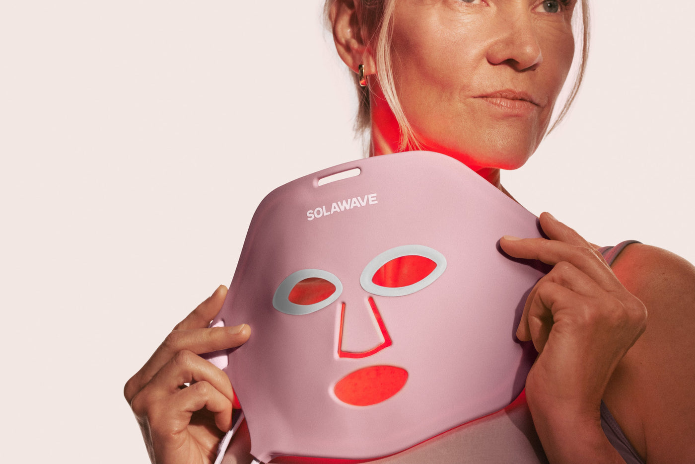 An image of a woman holding up a red light therapy face mask