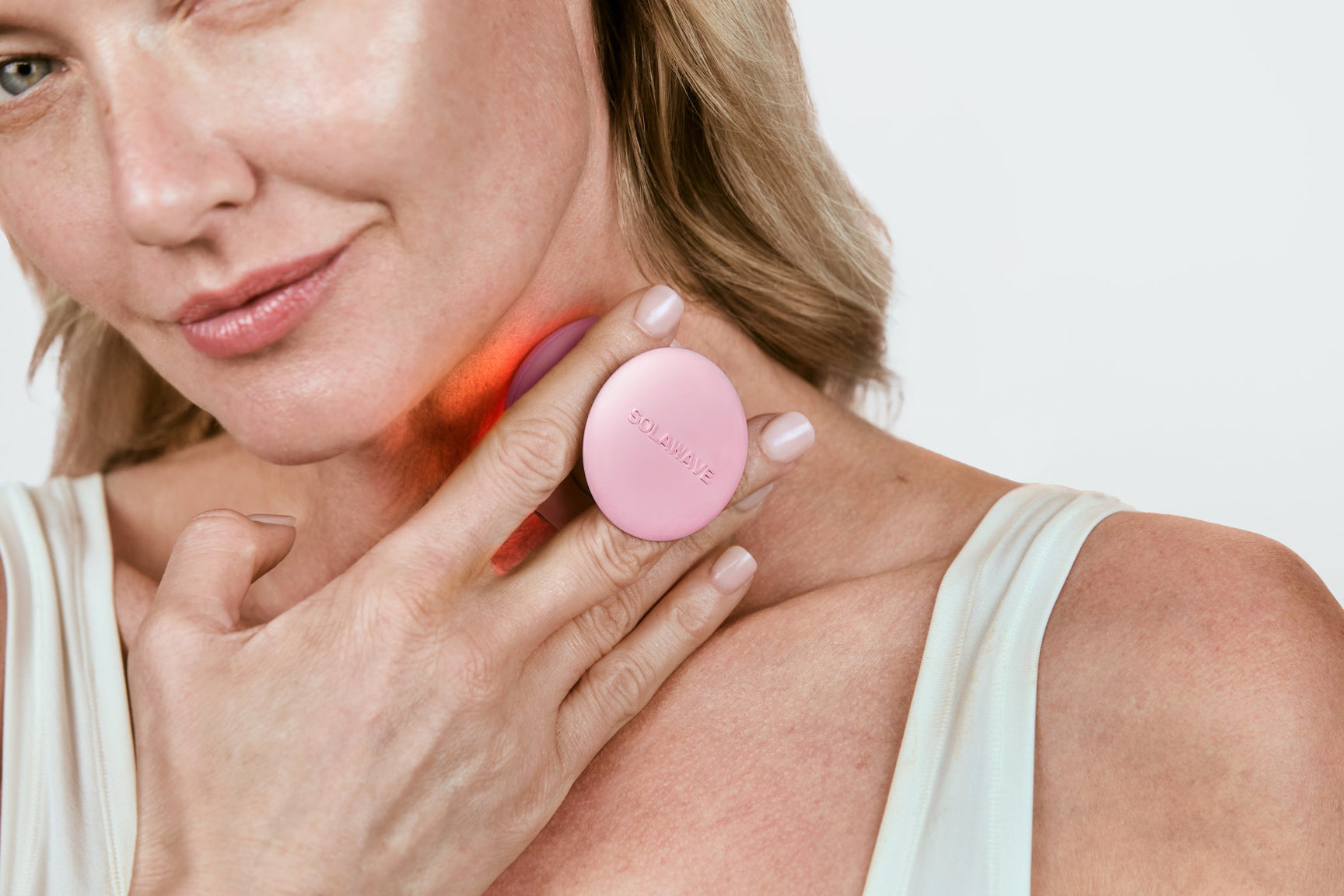 An image of a woman using a red light therapy device on her neck