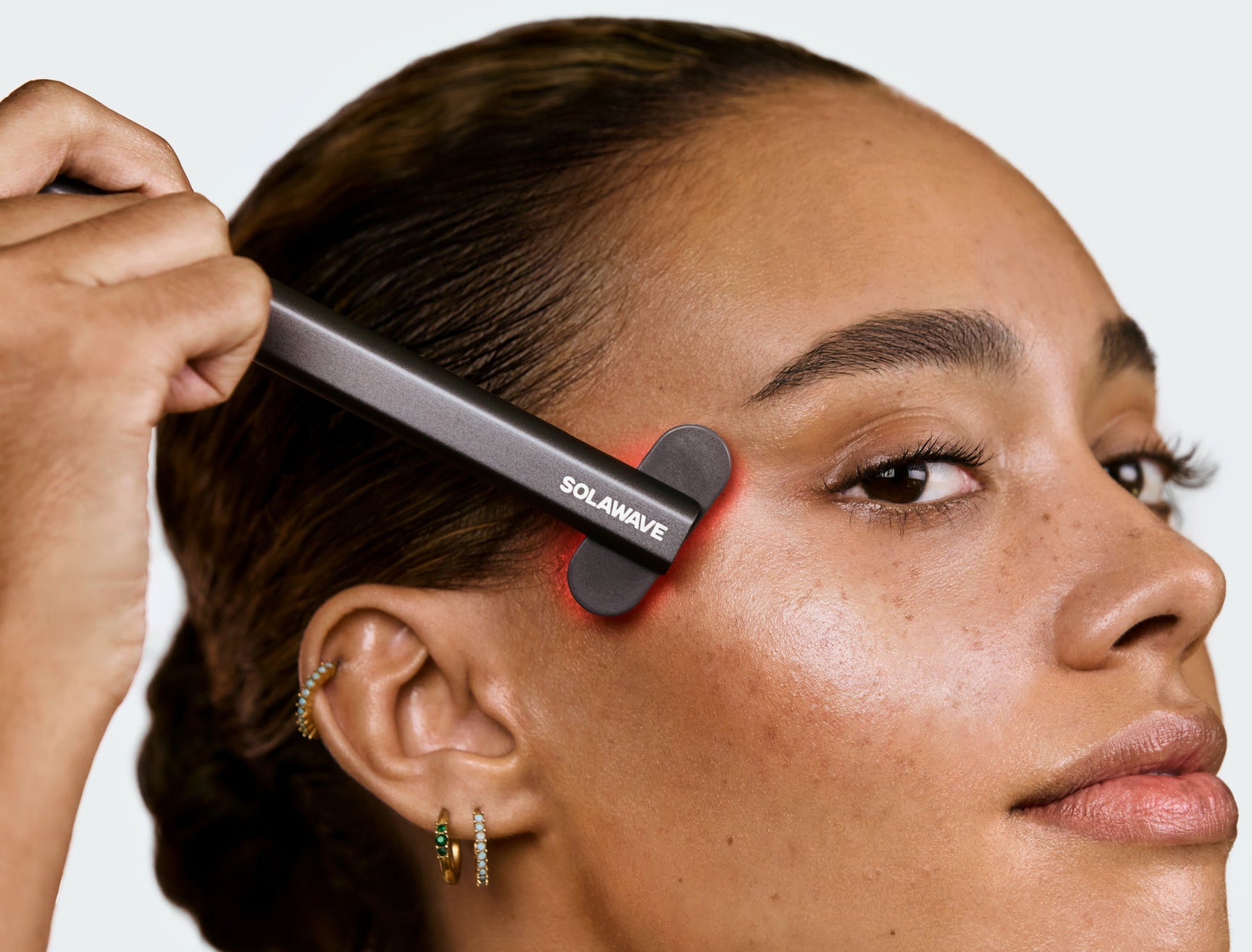 An image of a woman using a red light therapy wand on the side of her face