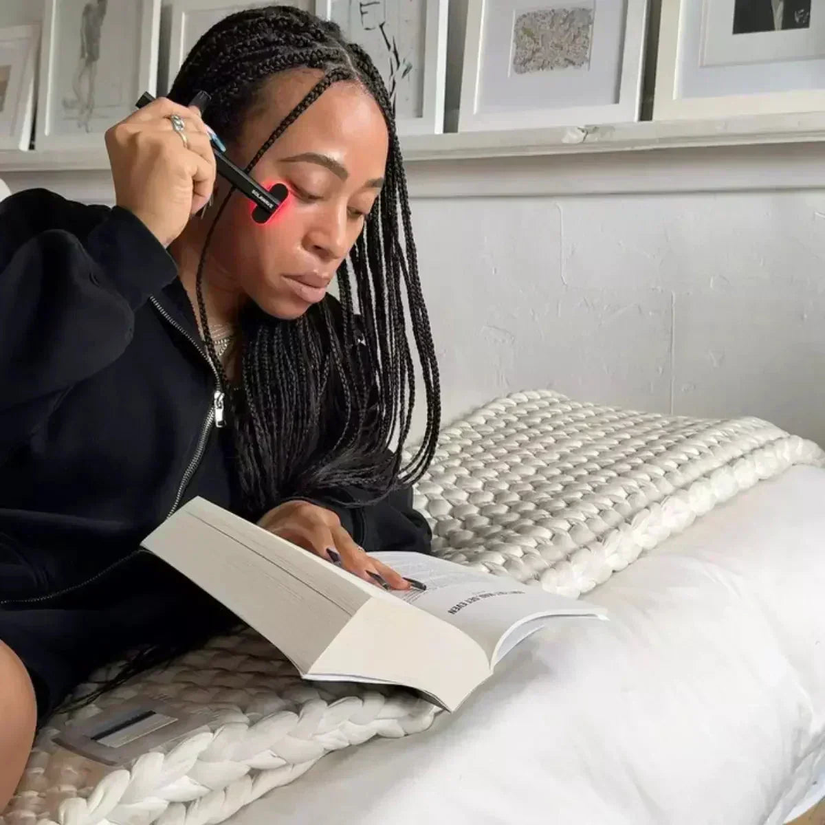 An image of a person reading a book and utilizing the Solawave red light therapy wand on their face