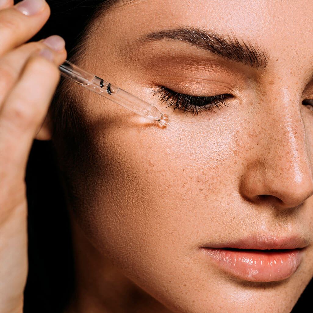 An image of a woman applying serum to her face to use with a red light therapy device