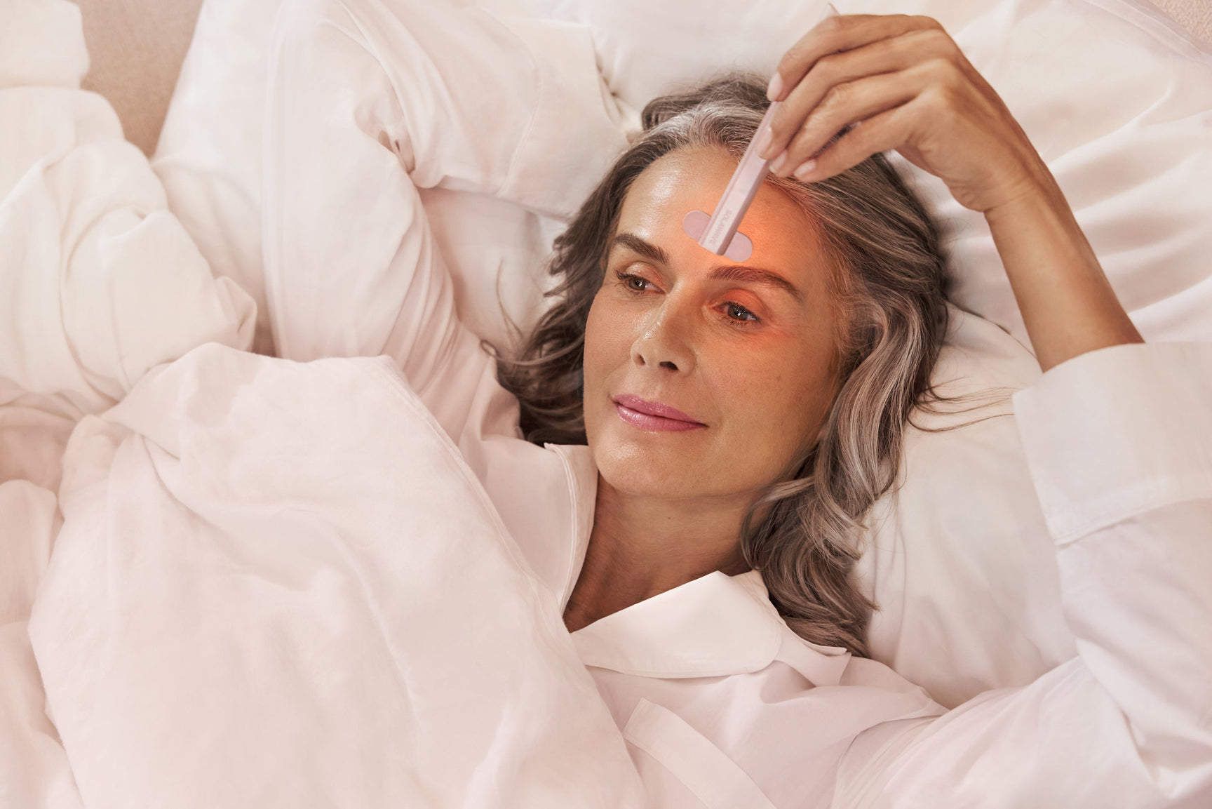 An image of a woman using red light therapy at home in her bed