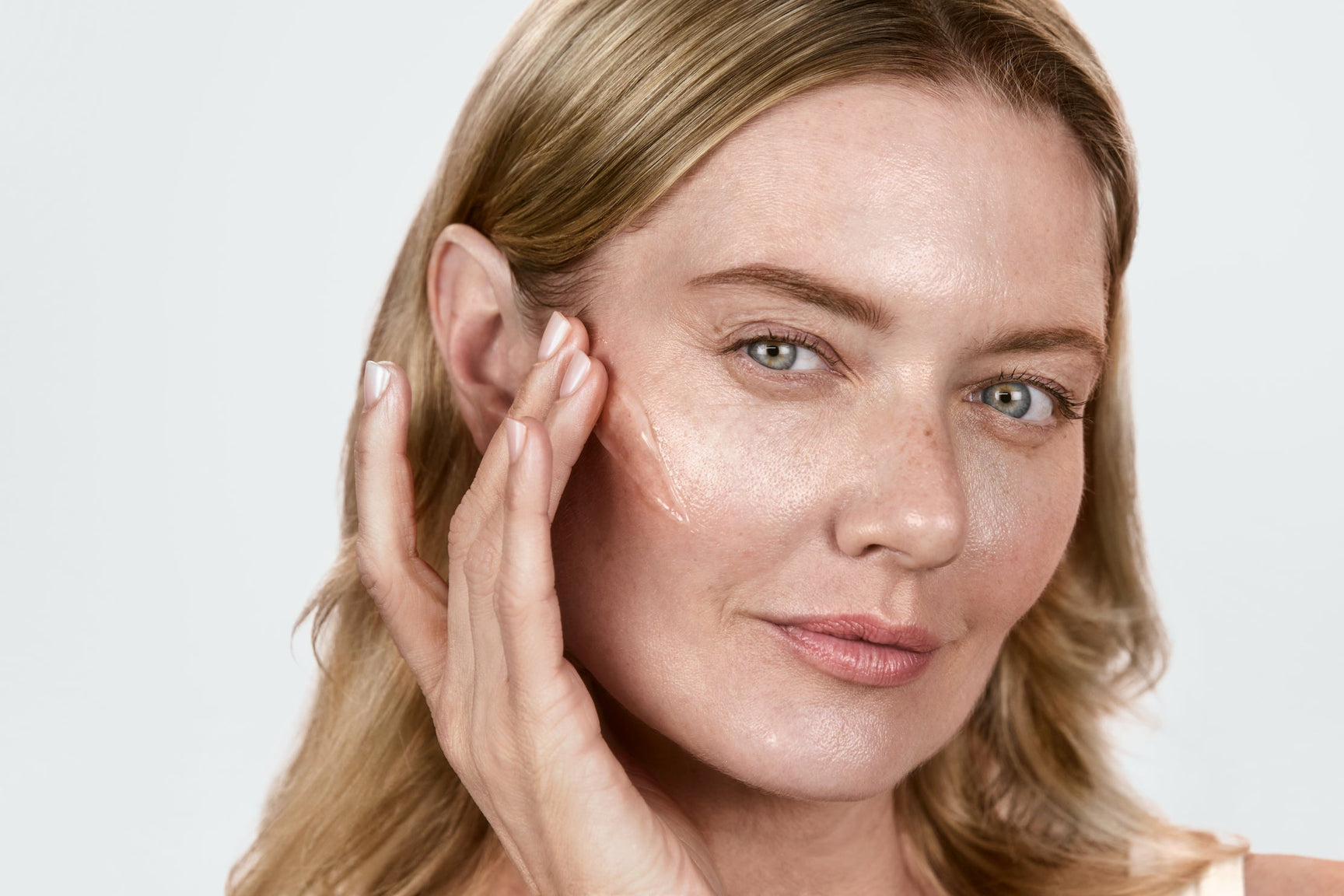 A woman applying lightboost serum to her face before red light therapy
