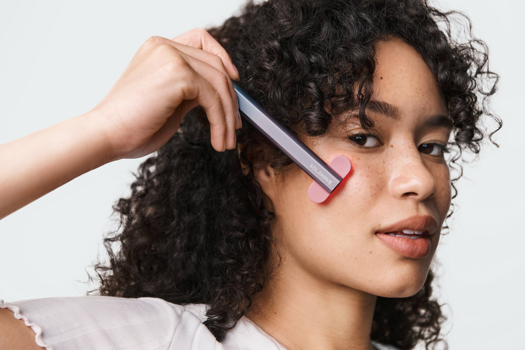 Woman using a red light therapy device on her cheeks