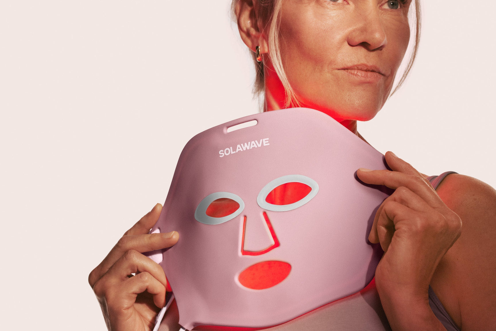 An image of a woman holding up a red light therapy face mask