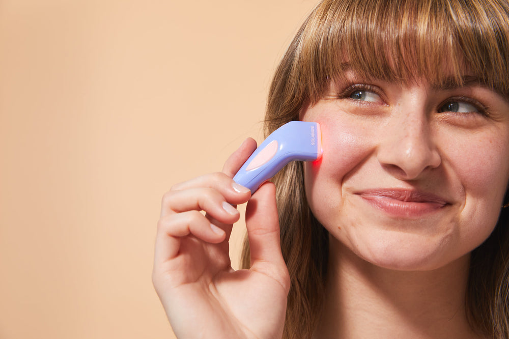 An image of a woman using a blue light therapy device on her face to target acne