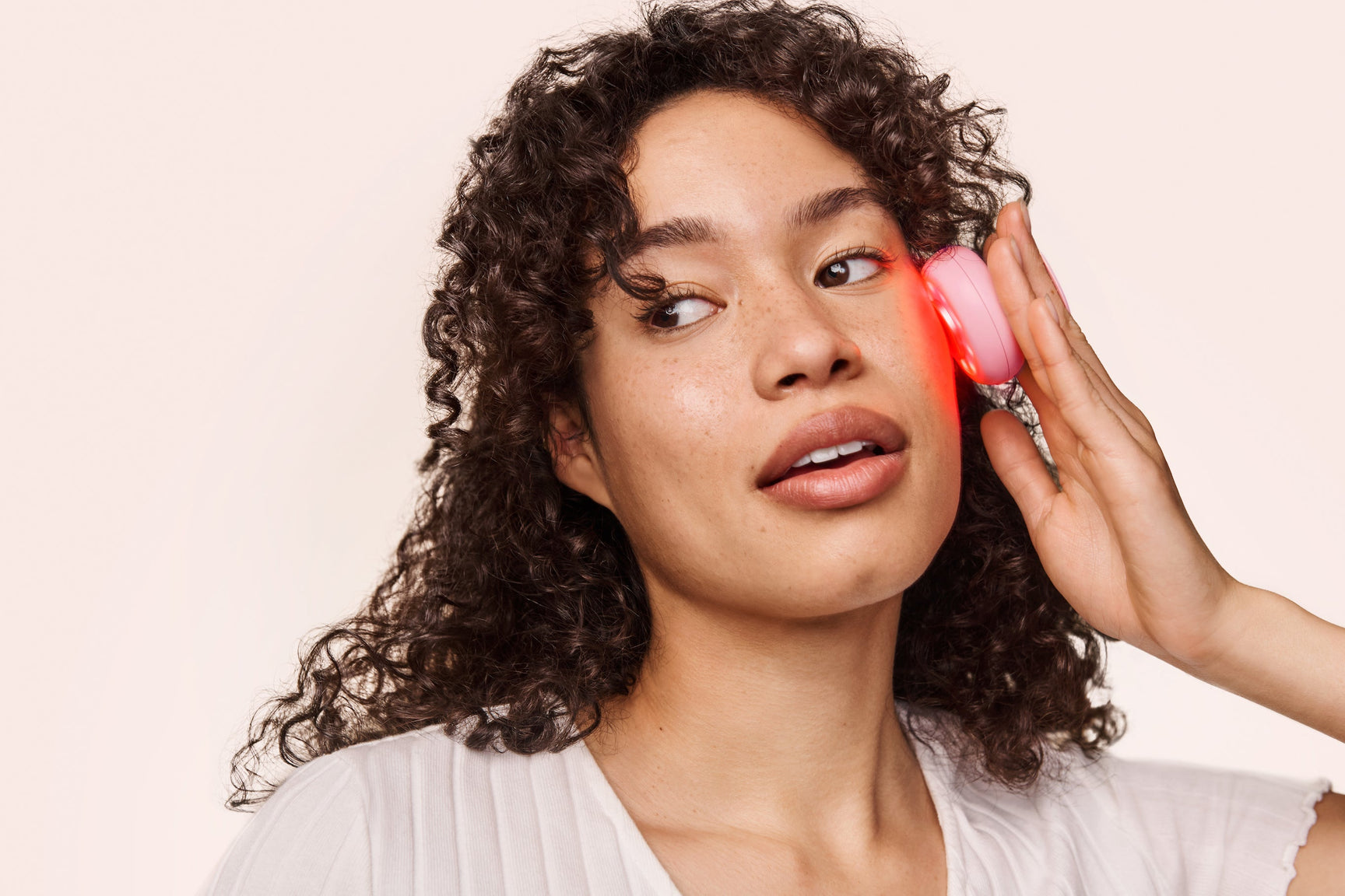 An image of a woman using the red light mini device on her face