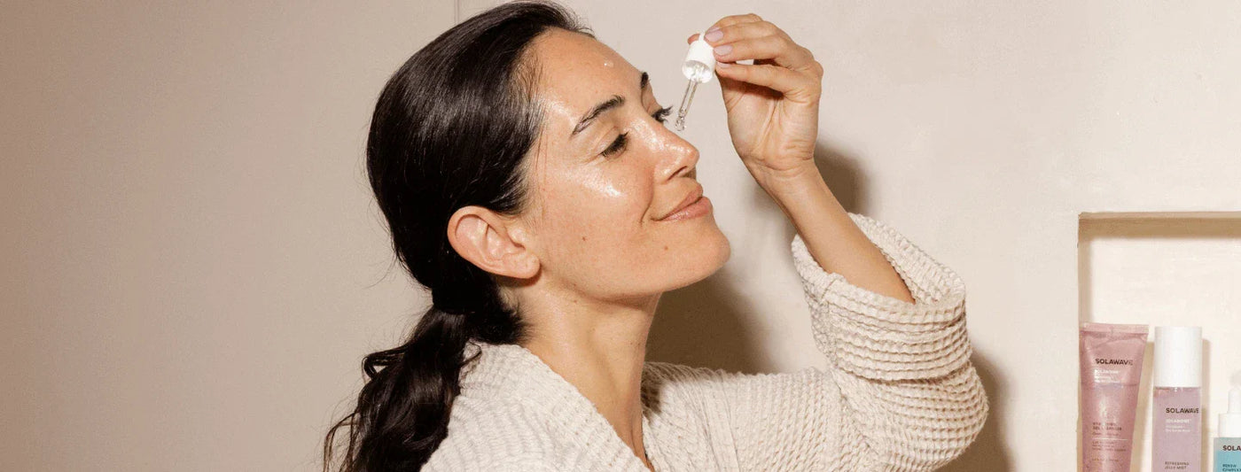 woman smiling while applying serum to face