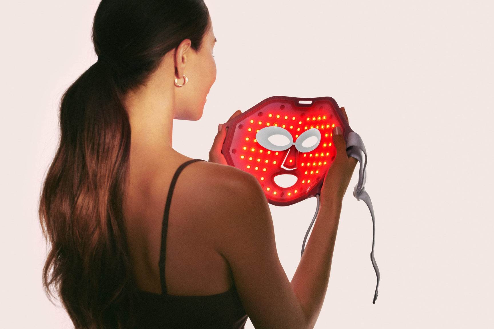 An image of a woman holding up a red light therapy face mask