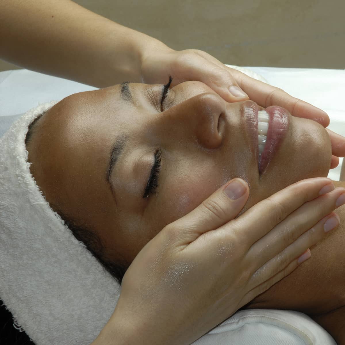 An image of a lady getting a facial massage and smiling