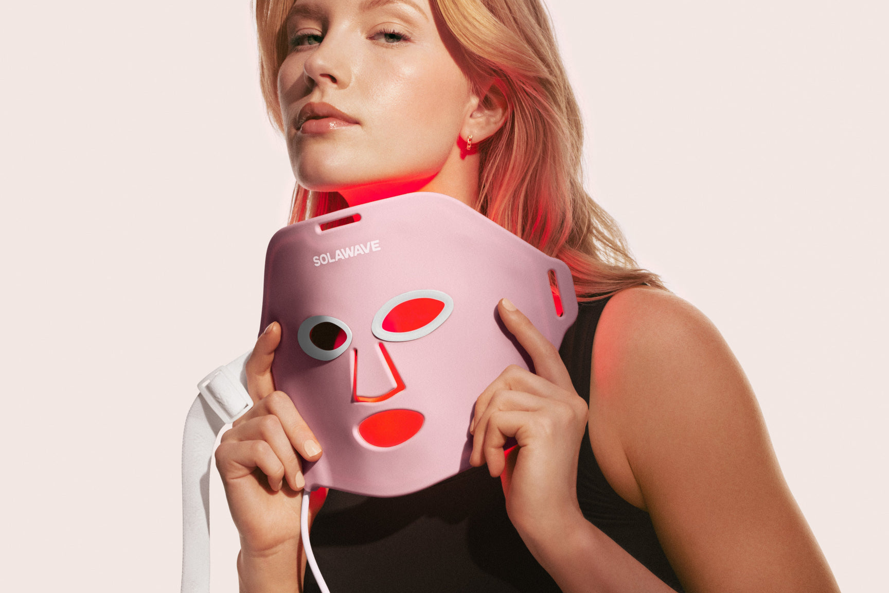 An image of a woman holding up a red light therapy face mask
