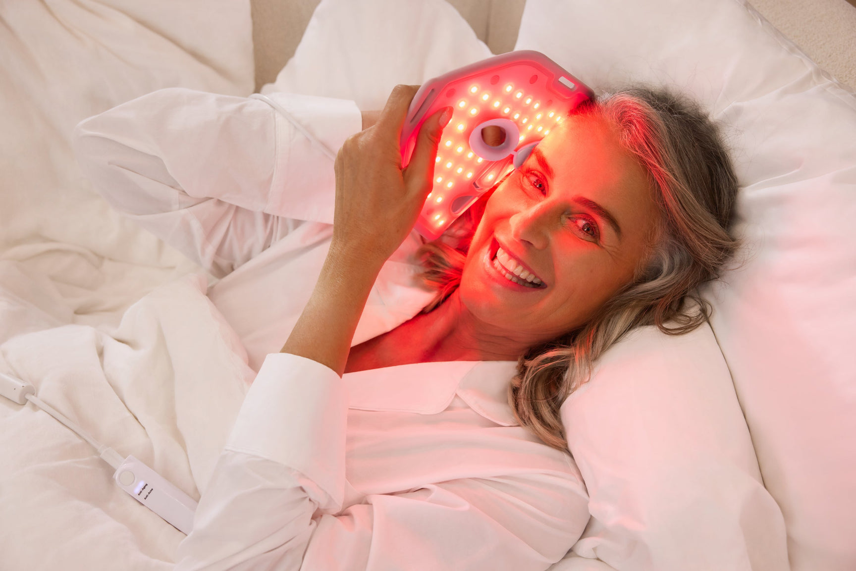 An image of an elderly woman using red light therapy face mask to target wrinkles