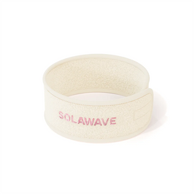 The Get Ready Headband by Solawave is a beige fleece headband with SOLAWAVE in pink on the front. Ideal for skincare routines, it features adjustable velcro for comfort and is displayed against a white background.