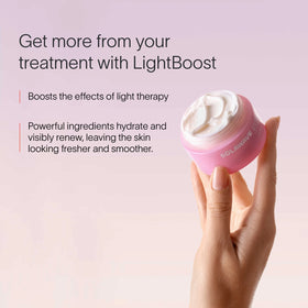 A hand holds a pink jar from the Neck & Chest LED Mask w/ LightBoost Cream Kit by Solawave against a soft pink background. Text reads: Enhance your routine with LightBoost. Boost red light therapy effects; powerful ingredients hydrate and renew, leaving skin looking fresher and smoother. || Rose