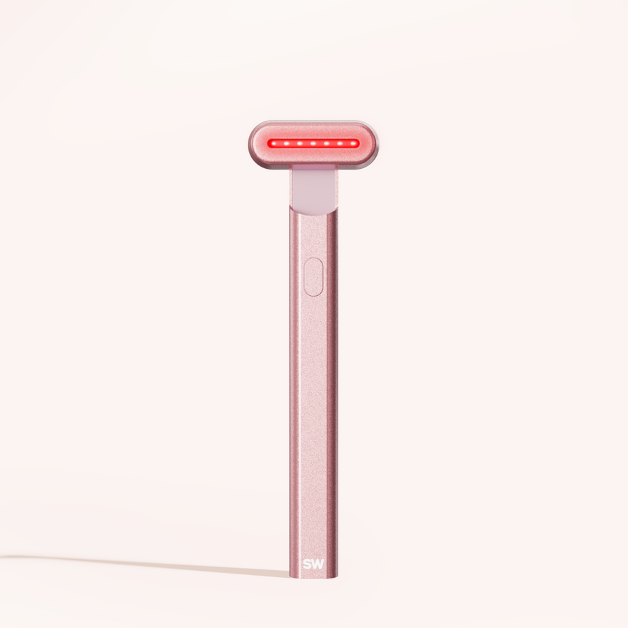 The Solawave 4-in-1 Radiant Renewal Skincare Wand Bundle, a sleek pink handheld device with a rectangular LED light head and single button, displays "SW" at the base and stands upright against a light background.
