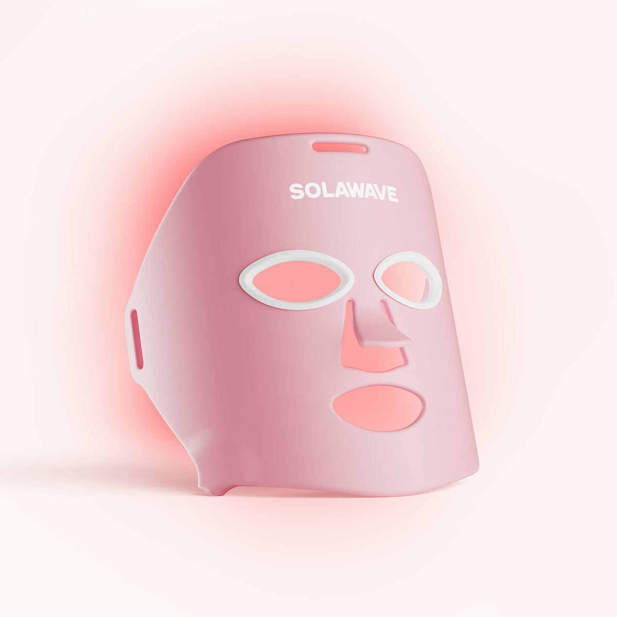 The Solawave Wrinkle Retreat Light Therapy Face Mask is pink with cutouts for the eyes, nose, and mouth. It emits a subtle red glow using red and near-infrared light therapy against a soft off-white background for anti-aging treatment. || Rose