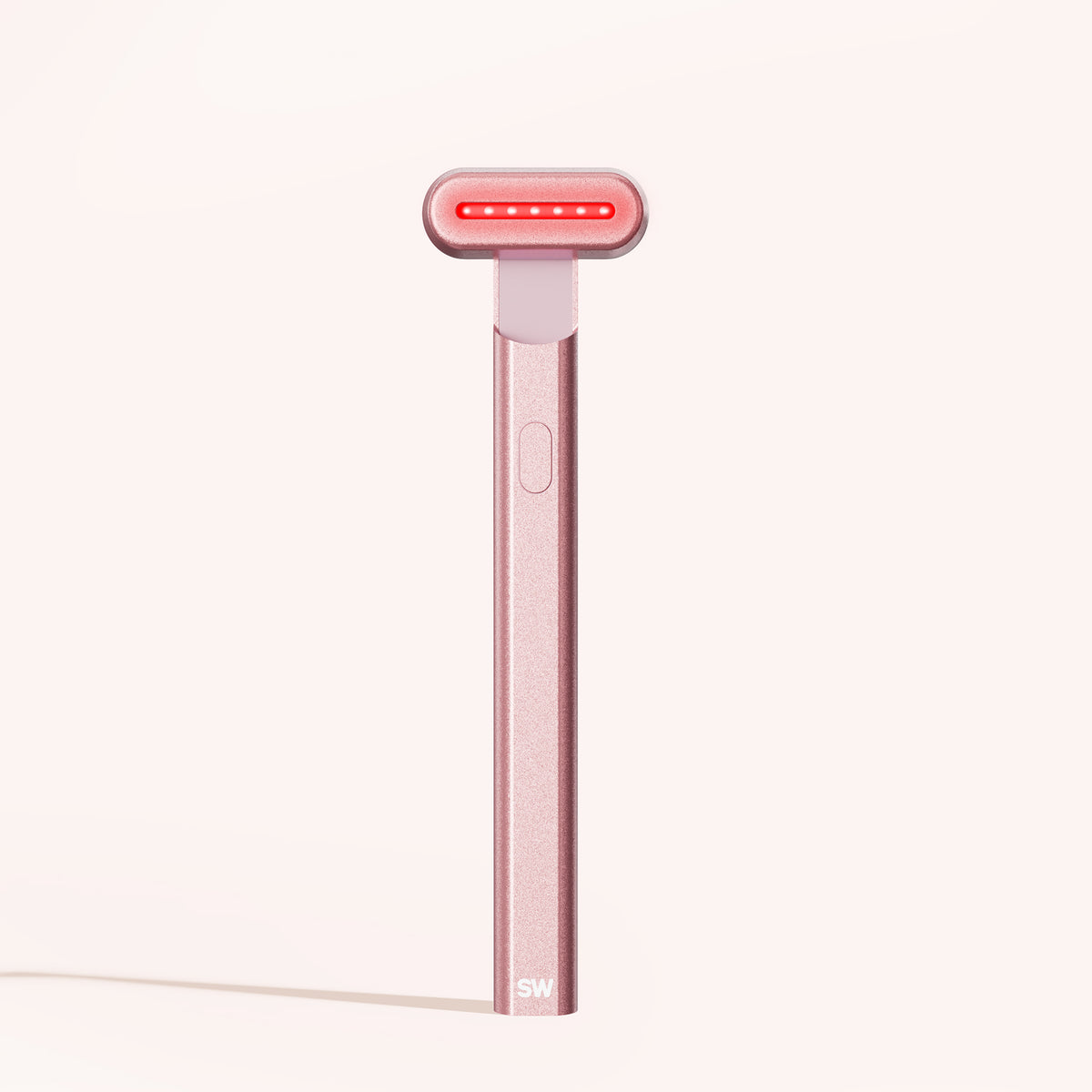 The 4-in-1 Radiant Renewal Skincare Wand from SolaWave boasts a metallic pink finish and cylindrical head, utilizing advanced technologies like a glowing red light bar. The handle features a discrete button and SW initials, promising to reduce fine lines against a pale beige backdrop.  || Rose Gold