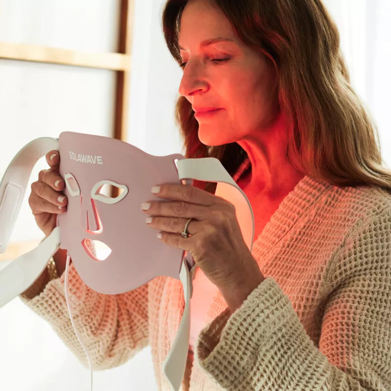 Woman holding the Solawave Wrinkle Retreat Pro LED Face Mask with its red light therapy panels glowing